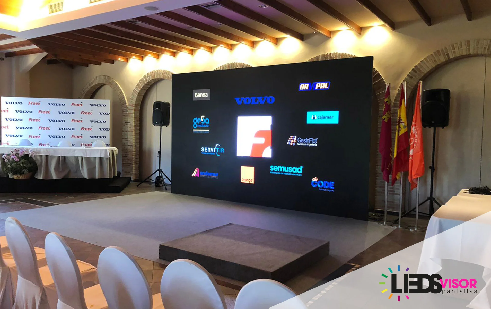 Sala de un acto corporativo con pantalla LED de fondo mostrando los logotipos del evento